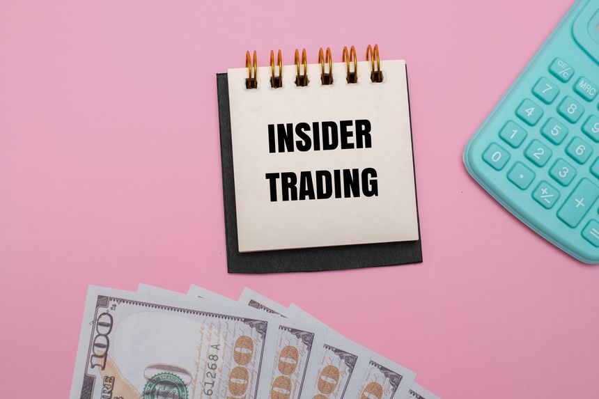 A notepad with INSIDER TRADING text, surrounded by 100-dollar bills and a calculator on a pink background. Symbolizing financial crime and illegal stock market gain