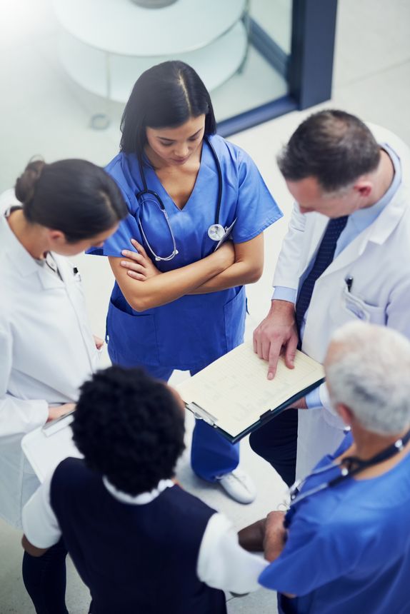Shot of a group of doctors talking together over a medical chart while standing in a hospital