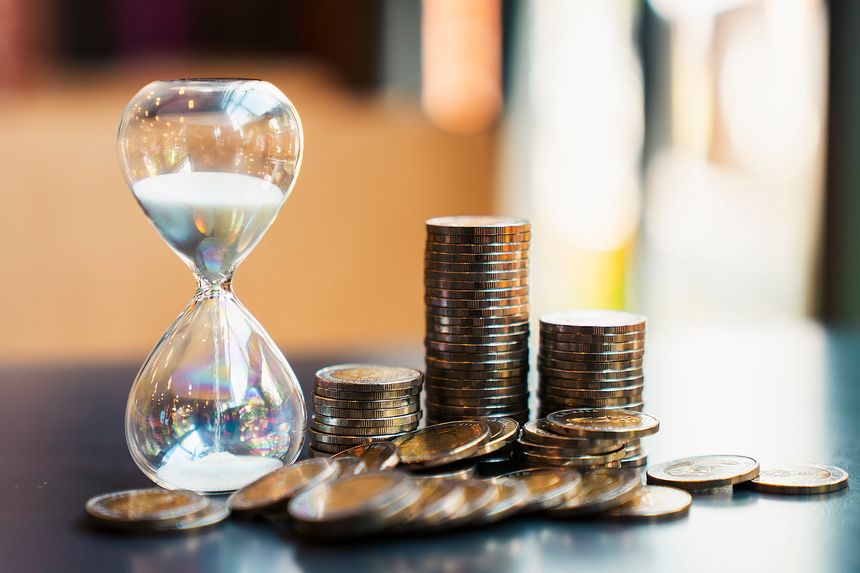 Hourglass and coin stacks on table against blurred bokeh background. Concept of time is money, long term financial investment, wealth management, retirement planning, and business profit growth.