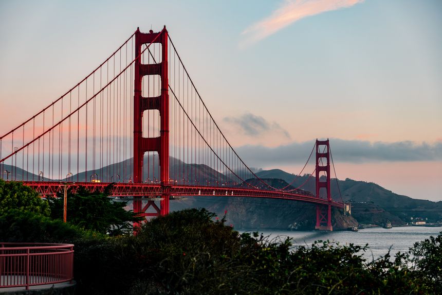 The iconic Golden Gate Bridge stands majestically against a soft twilight sky, its signature red hue prominent over San Francisco Bay.