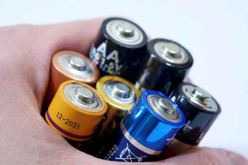Hand holding mixed AA batteries, extreme closeup of colorful household cells with visible positive terminals, portable power, energy storage, recycling and e-waste disposal concept on white background