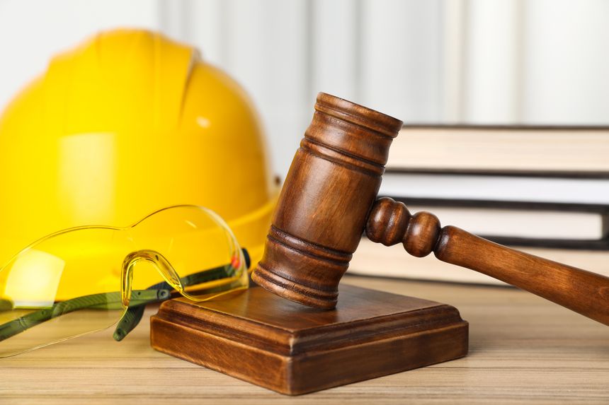 Accident at work. Gavel, goggles, hardhat and stack of books on wooden table, closeup