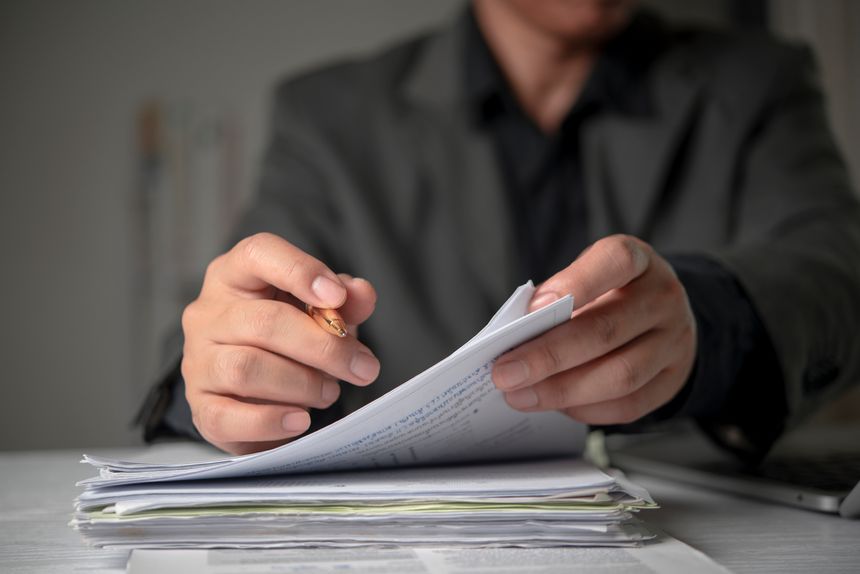 Close up hands lawyer reading studying contract paperwork holding pen desk. Corporate business administration paperwork overwhelming workload legal review verification concept.