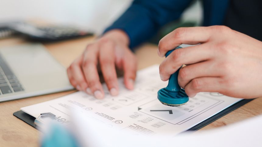 Business professional stamping approved document with official seal at office desk. Concept of contract approval, legal authorization, compliance verification.
