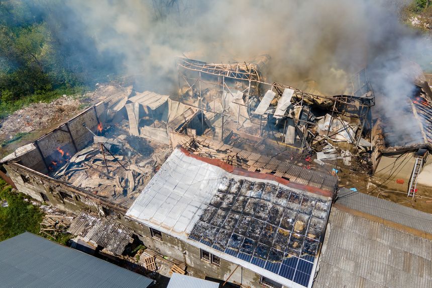 Aerial view of ruined building on fire with collapsed roof and rising dark smoke.