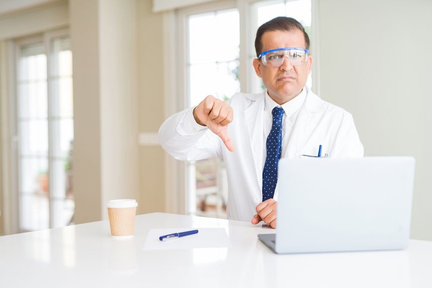Middle age scientist man wearing professional glasses working using laptop with angry face, negative sign showing dislike with thumbs down, rejection concept