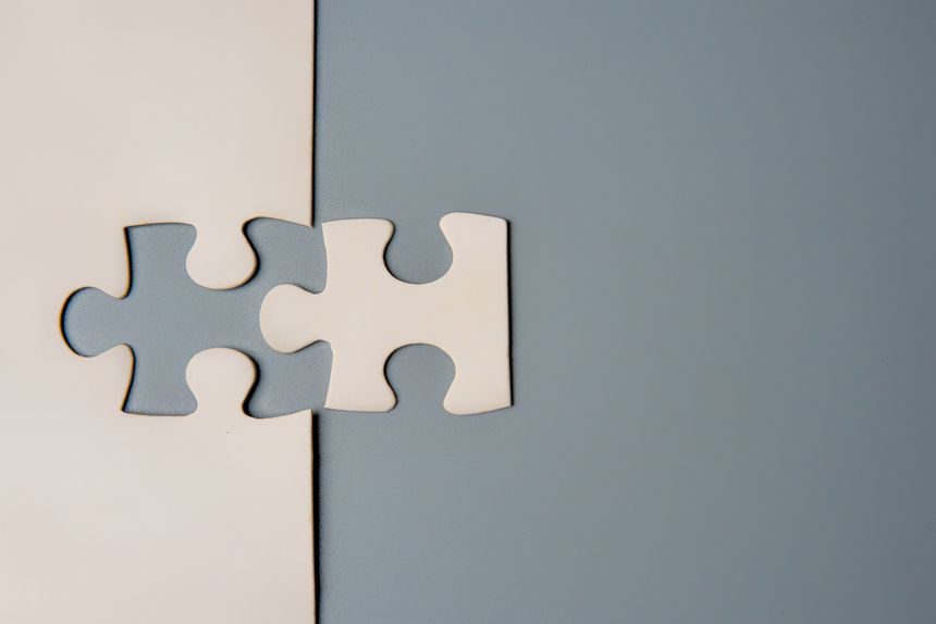 Two puzzle pieces connecting, one white and one grey, on a contrasting background, symbolizing unity, connection, and collaboration. Copy space for text.
