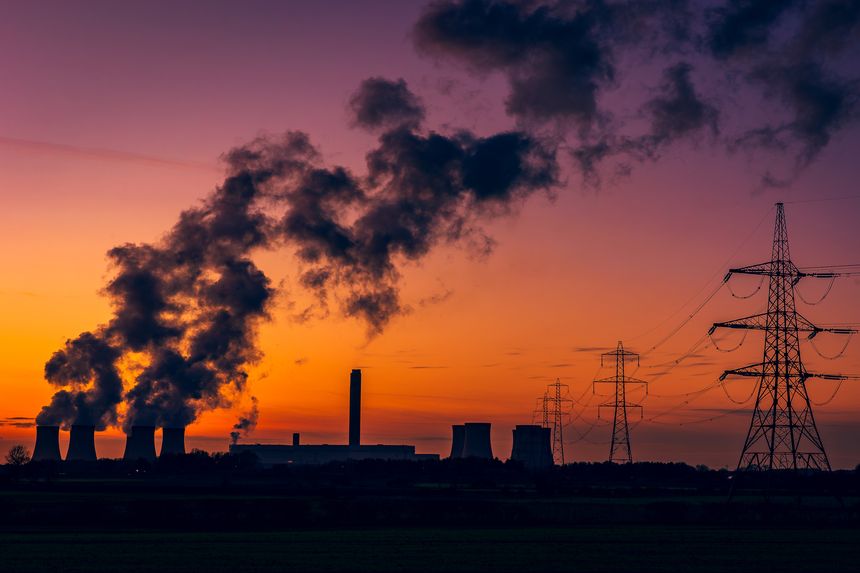 Silhouette of a power station's cooling towers against a beautiful Winter's sunset near Drax in North Yorkshire, UK, with electricity pylons and plumes of water vapour rising from the cooling towers. Horizonal. Copy space.