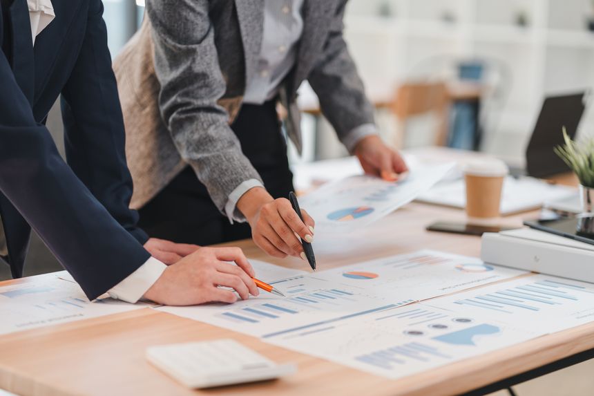 A Two business professionals analyzing financial charts and graphs on wooden desk in modern office setting, collaborating on project with focus and teamwork