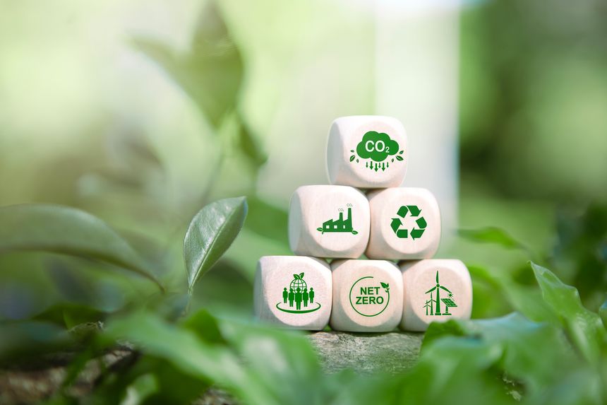 Wooden blocks with eco-friendly icons representing CO2 reduction, recycling, renewable energy, and net zero goals placed on green leaves, symbolizing sustainability, environmental responsibility, and clean energy solutions.