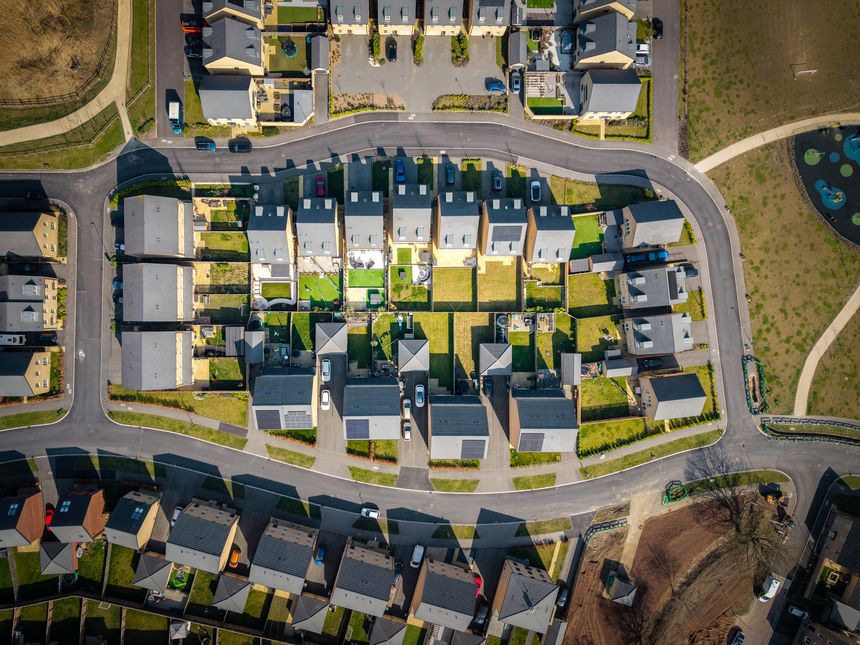 Aerial top down view above a block of newly built affordable suburban homes in the UK with small gardens and built on green belt land due to a housing shortage
