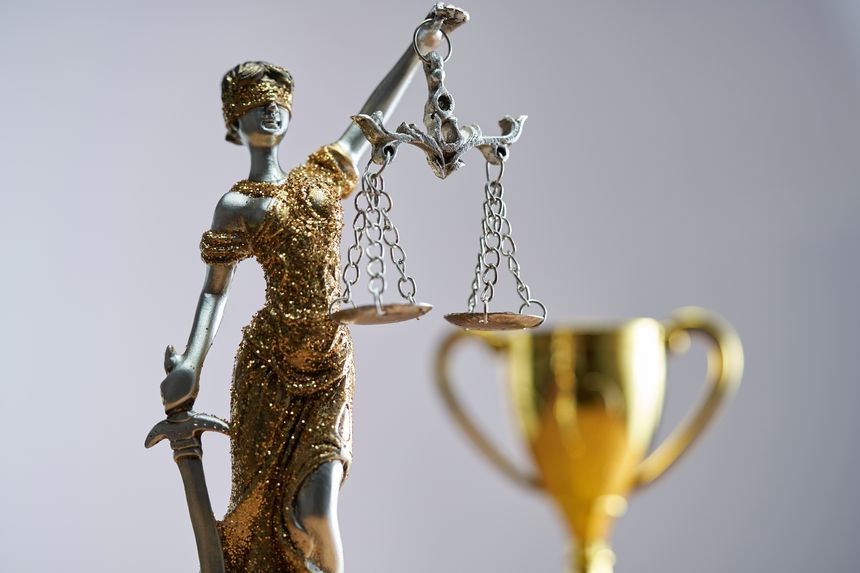Statue of Lady Justice with gold trophy against white background