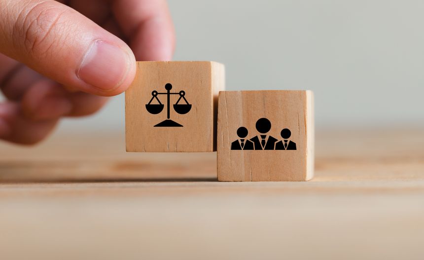 Close-up of wooden blocks showing justice scales and business people icons, symbolizing the relationship between law and corporate governance, teamwork, and ethics.