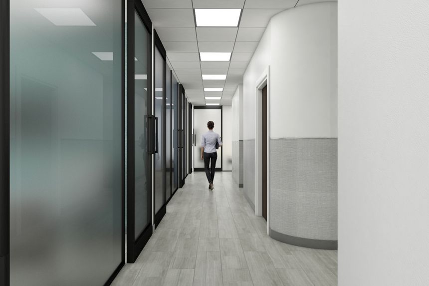 A clean and modern office corridor with large windows and a single individual walking. The bright environment emphasizes professionalism and contemporary architecture in a workplace setting.