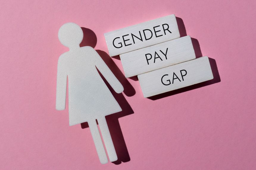 A female icon next to three white wooden blocks with the text GENDER PAY GAP on a pink background. Economic inequality and social rights concepts.