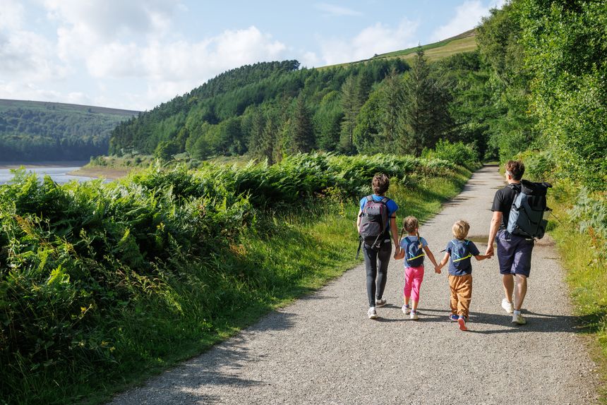 Two parents with their kids enjoy a walk on a picturesque dirt road, flanked by dense forest, open landscapes Howden reservoir and dam, England