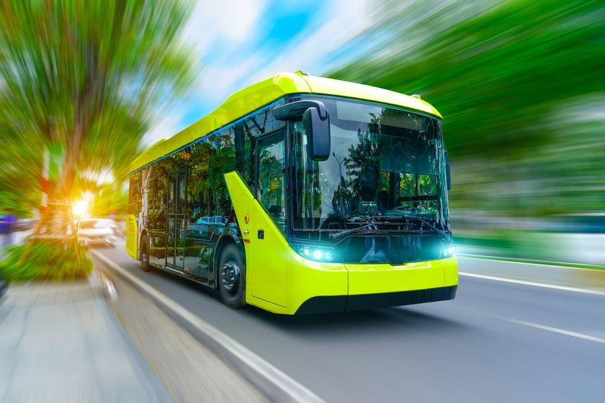 Electric bus with headlights on drive down the street in motion blur speed effect among trees.