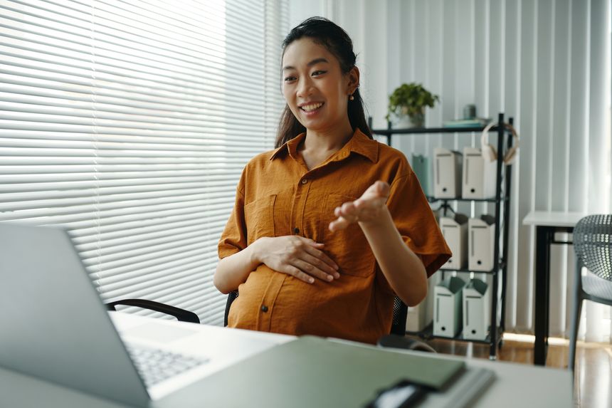 Asian woman smiling while participating in video call at home office with natural lighting and green plant in background, creating a serene and productive atmosphere