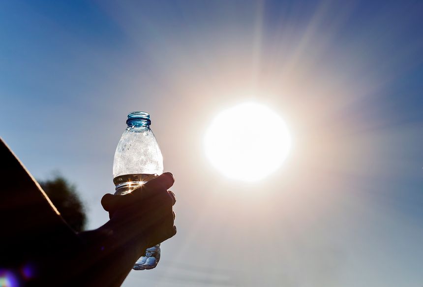 Bottle with water in a woman's hand against bright sun outdoors. Climate change hotness concept