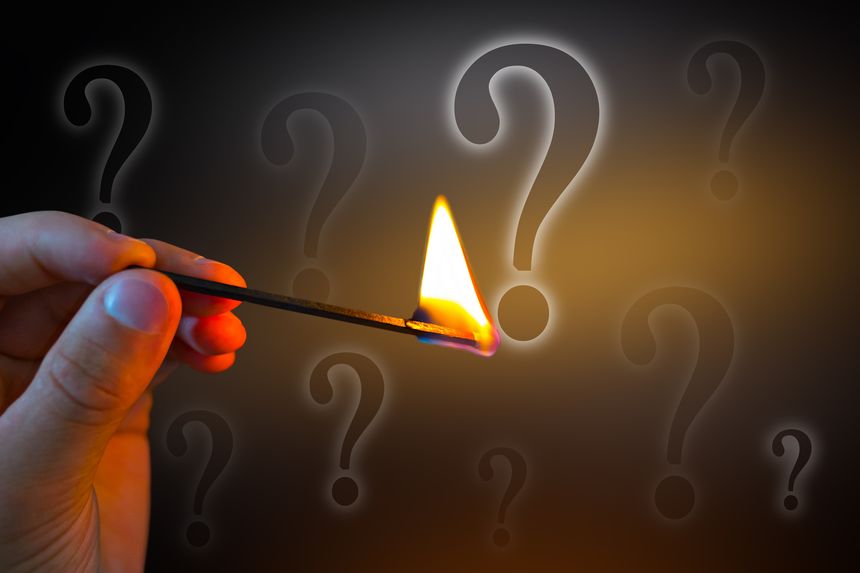 Burning match in human hand and question mark close up. The concept of global catastrophe.