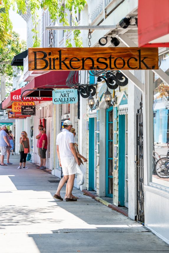 Key West, USA - May 1, 2018: Restaurants, cafe, Guild hall art gallery studio, stores, Birkenstock shoes shop, store on Duval street road, people, tourists walking on sidewalk in summer, Florida city