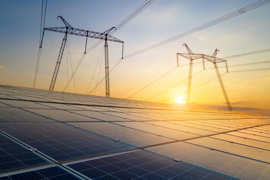 High voltage towers with electric power lines transfering energy from solar photovoltaic panels at sunset. Production of sustainable electricity concept.