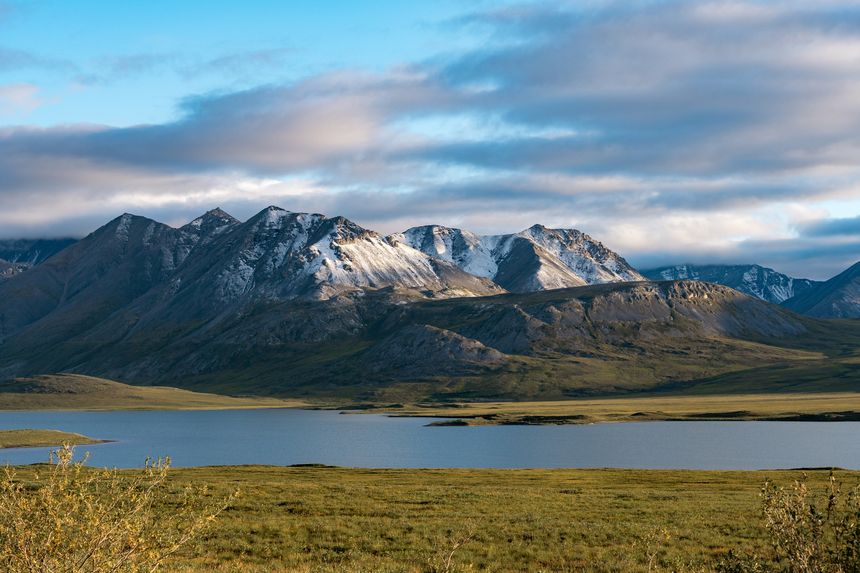 View Of Galbraith Lake With Towering Snow Dusted Mountains Of The Brooks Range In Alaska On A Sunny Day In August From The Dalton Highway