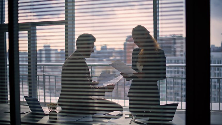 Manager silhouette talking executive at panorama window cabinet. Unrecognized finance analysts checking reading report papers at dark room. Anonymous subordinate woman assisting boss in cityscape