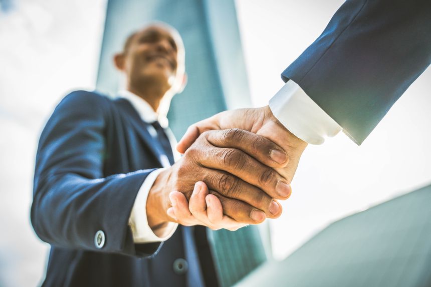 Two business men shaking hands in front of office building outdoors - Concept about leadership, agreement, teamwork and business