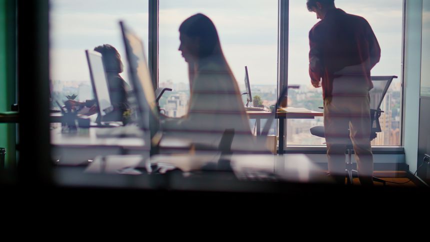 Corporate workers silhouettes typing computers in modern tech studio. Team of focused people debugging code. Open office with city panorama. Busy digital workflow and project development activities
