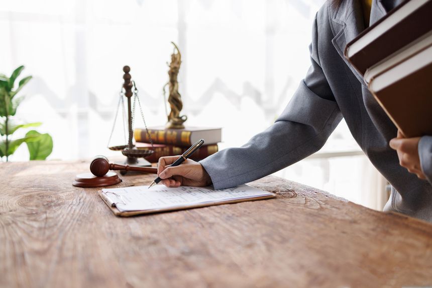 Lawyer's hand writing important legal documents on a wooden office desk