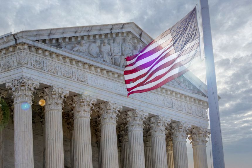 The sun peaks through clouds to stream through American Flag outside of the United STates Supreme Court