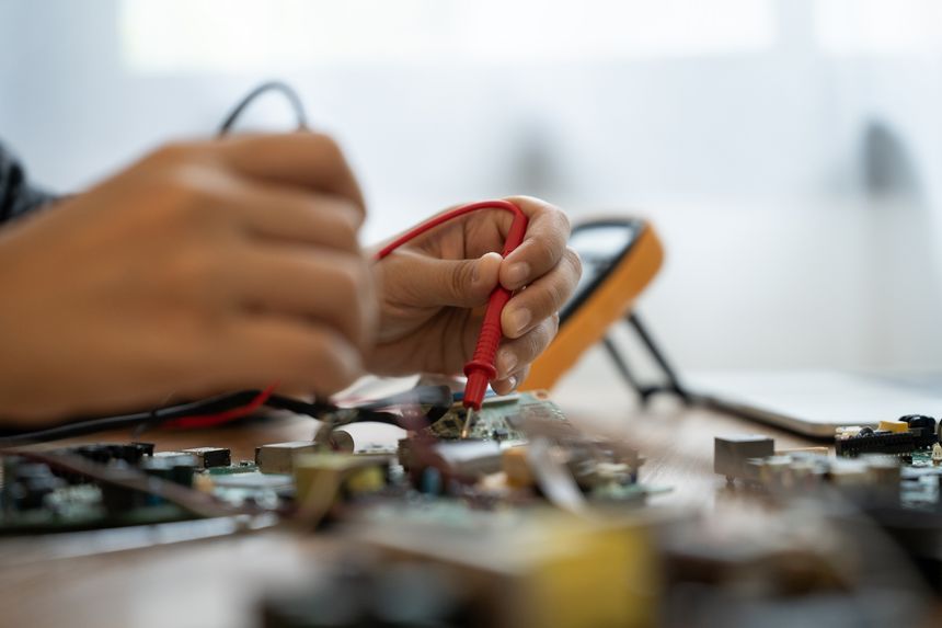 A person is working on a computer part, writing on a piece of paper. Scene is focused and determined