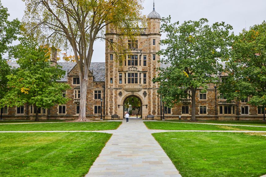 Gothic-style University of Michigan building on verdant campus, Ann Arbor, person walking through archway