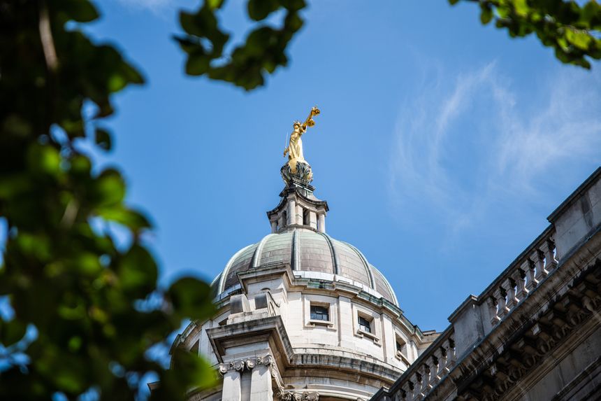 Looking up at the golden statue of Lady Justice atop the Central Criminal Court in London, set against a bright blue summer sky.