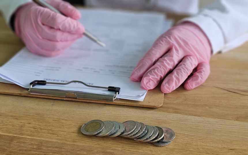 Person wearing pink gloves writing notes while coins are placed on a wooden table during a transaction or assessment
