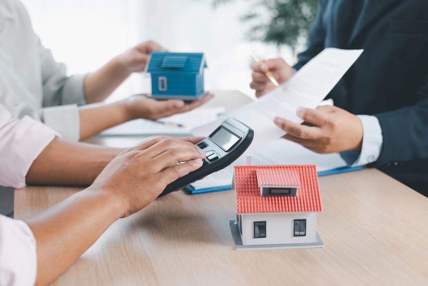 House model on desk with blurred people discussing contract in background, concept of real estate investment, mortgage loan, home ownership, property business and financial agreement.