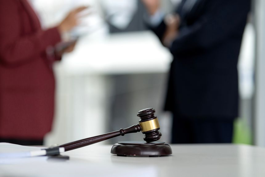 Authority and legal power represented by a classic gavel on a white table. Blurred adult professionals consult on important matters.