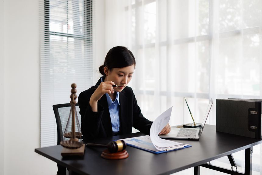 Female lawyer at desk reviewing documents with scales of justice and gavel, focused on legal strategy and professional advocacy in a modern office setting for business law
