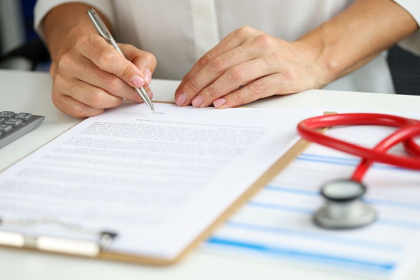 Close-up of female doctor in medical gown put sign on clipboard with documents. Qualified worker made prescription for patient. Medicine, clinic concept
