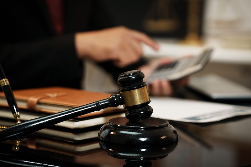 Close-up of judge gavel on desk with blurred lawyer calculating bills, symbolizing legal decision, justice, court, finance and litigation.