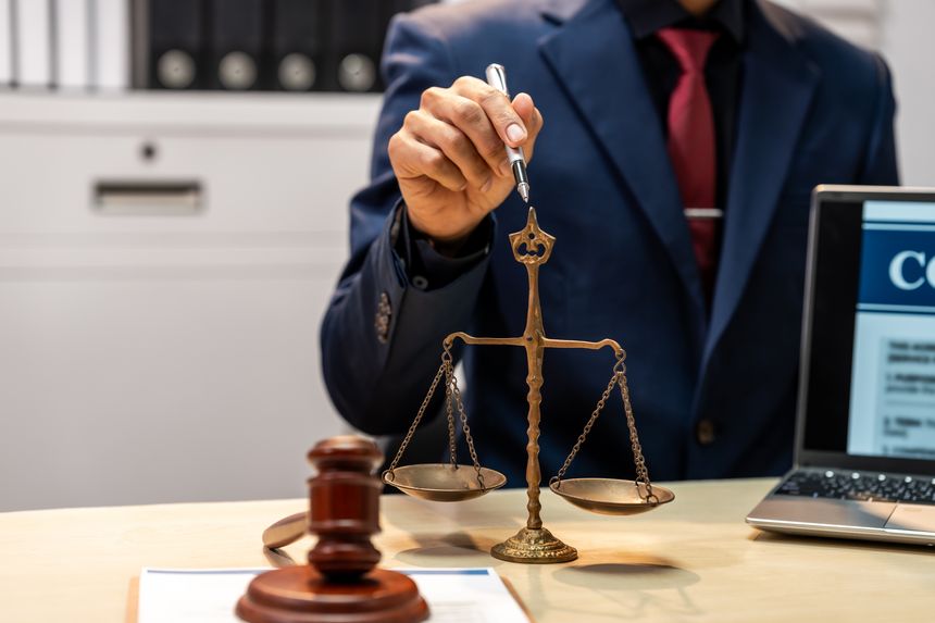 Business professional holding a pen near scales of justice with gavel and laptop on desk in a law office