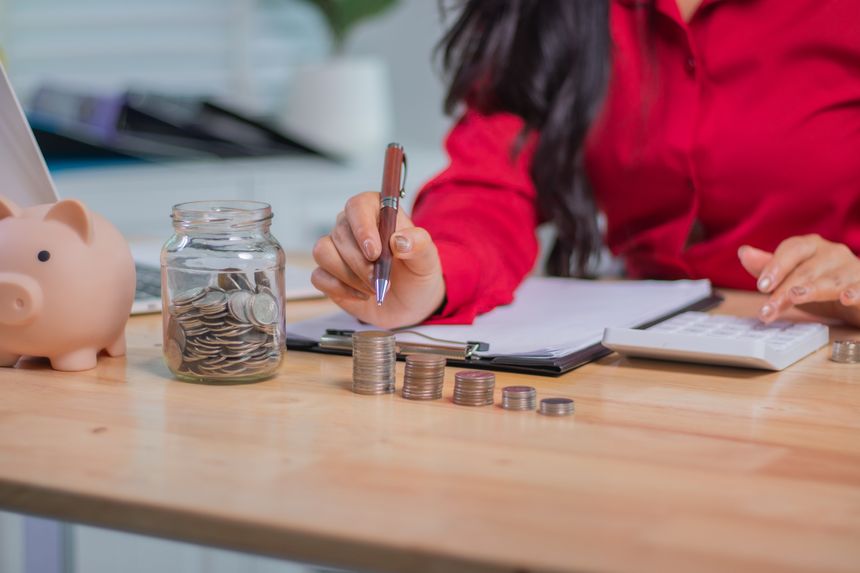 A middle-aged businesswoman sits indoors in the sunshine, smiling with satisfaction, thinking about finances, saving, investing and retirement planning for a successful future.