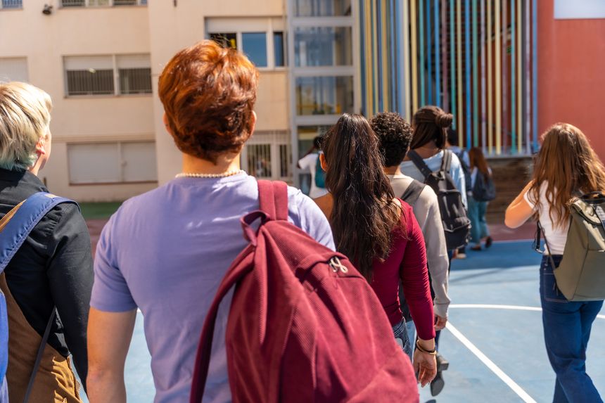 Group of young adult and teenage students walking together with backpacks on a university campus or school playground, moving towards a building, representing education and friendship