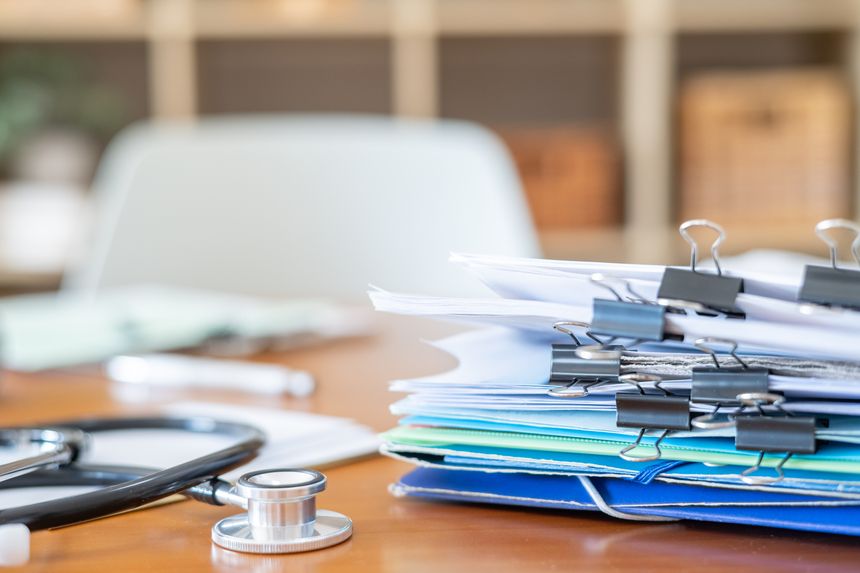 Stethoscope resting on a wooden desk next to a stack of patient files. Papers. And folders. Symbolizing healthcare administration. Patient records