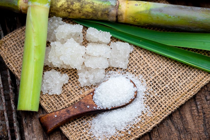 Fresh sugarcane stalks and raw sugar crystals representing India's sugar industry and the rising price of sugar in the Indian market.
