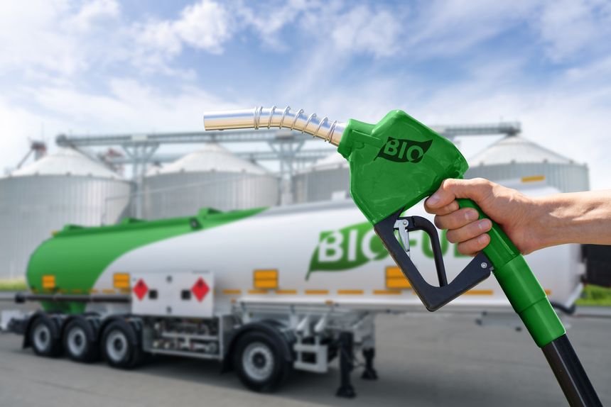 Hand with fuel nozzle with inscription BIO on a background of tank trailer with biofuel. Carbon neutral bio fuel decarbonization concept.