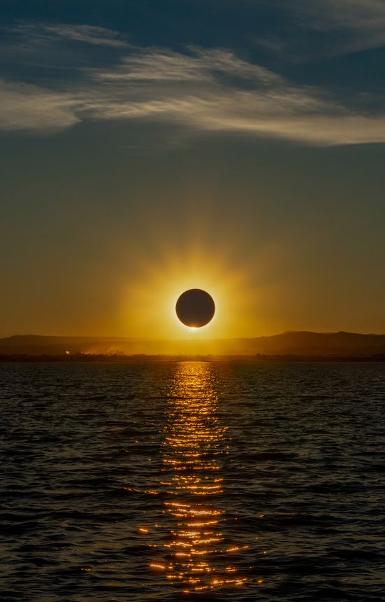 Total solar eclipse over a coastal lagoon at sunset with a spectacular reflection of the sun in the water in the Albufera of Valencia, Spain.