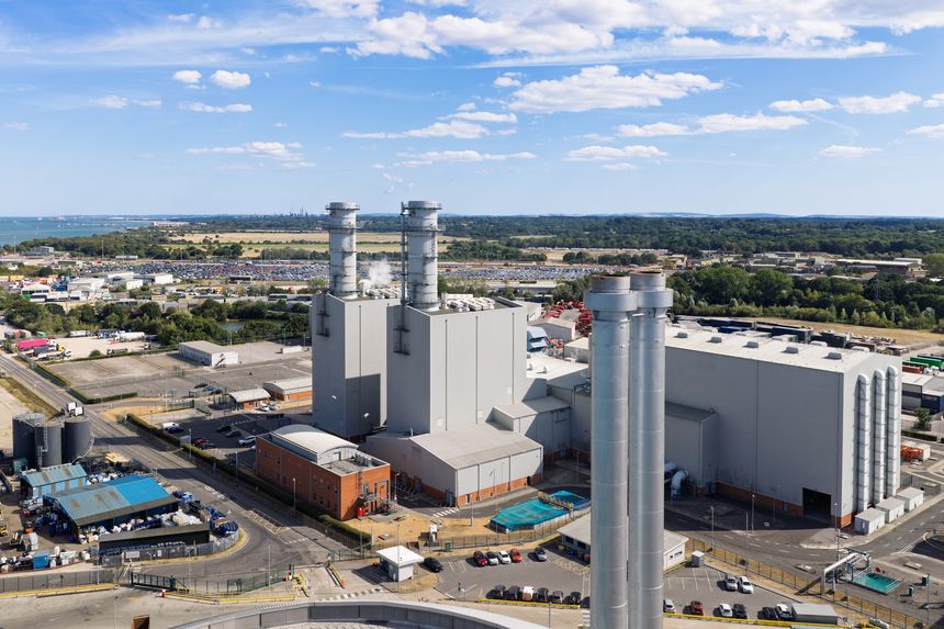 Large industrial power plant generating electricity using natural gas turbines on a sunny afternoon in a coastal region with green landscapes and clear blue sky during daylight hours