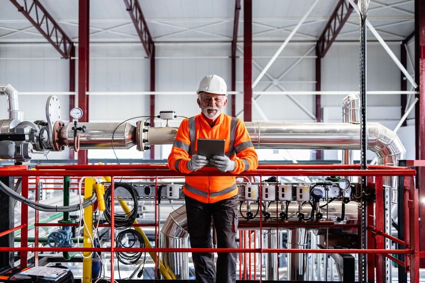 Senior engineer standing on platform holding digital tablet at a petrochemical plant